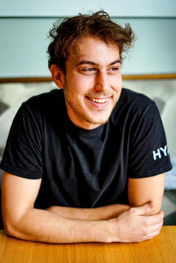 Koch Jassin Karch sitzt an Tisch und lächelt.